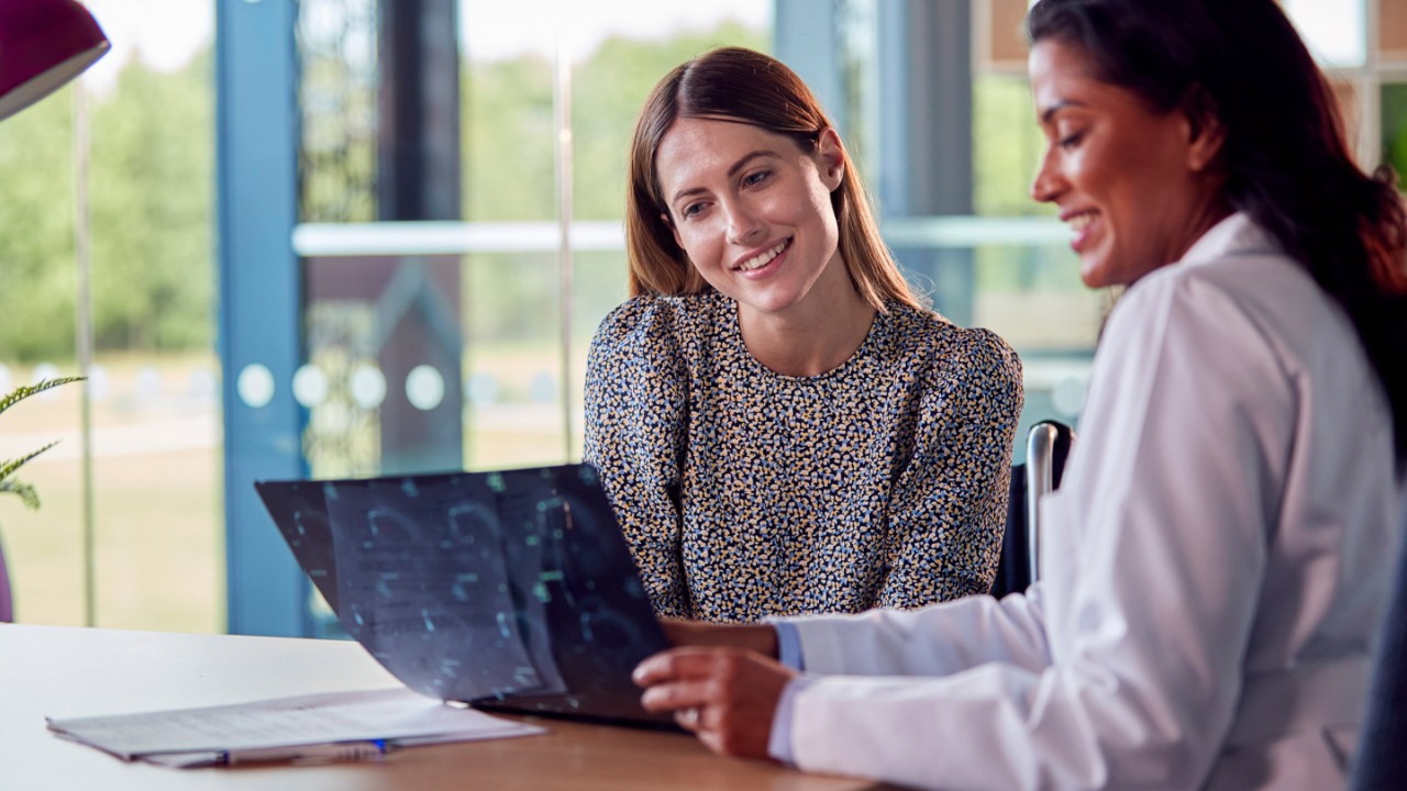 Female Doctor Discussing Scan Results With Smiling Woman Patient In Hospital